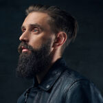 Close up portrait of bearded male wearing black leather jacket. ducktail shave | beard style